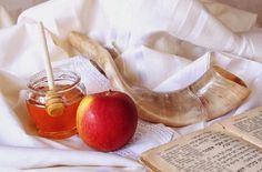 an apple and honey sit on a bed next to some old book pages, with a wooden shoe in the background