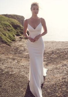 a woman in a white dress is standing on the rocks by the water and looking at the camera