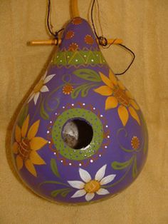 a purple birdhouse with yellow flowers painted on it's sides and a cat in the hole