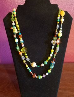 "This necklace is perfect for nature and wildlife lovers.  It features a tropical bird and has corresponding colors and is a wrap necklace that is 46\" in length.  It is bright and fun with yellows, greens, and blues.   Materials: wood, re-purposed beads,  polished stones, silver, plastic beads, glass beads  I began making jewelry in 2007 when I was living in Korea.  I was out shopping one day and found a carved jade piece that I fell in love with.  I thought it would look great on a necklace, s Nature-inspired Multicolor Beaded Necklaces As Gift, Multicolor Beaded Necklaces With Nature-inspired Style, Adjustable Yellow Lariat Necklace, Unique Long Yellow Necklace, Unique Adjustable Multicolor Long Necklace, Adjustable Whimsical Green Necklace, Whimsical Multicolor Beach Necklace, Yellow Single Strand Bohemian Necklace, Unique Yellow Necklaces For Beach