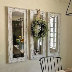 three mirrors hanging on the wall above a dining room table with a wreath and potted plant