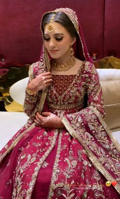 a woman in a red and gold bridal gown sitting on a white couch with her hands together