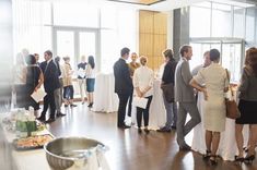 a group of people standing in a room with food and drinks on the table,