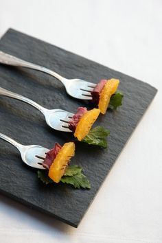 three forks with food on them are sitting on a black slate board, ready to be eaten