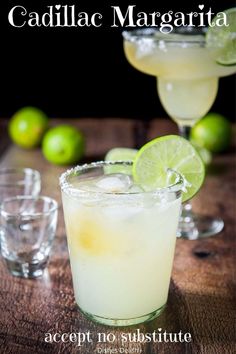 two margarita cocktails sitting on top of a wooden table next to lime wedges