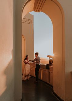 a man and woman are standing in an archway holding each other's hands as the sun sets behind them