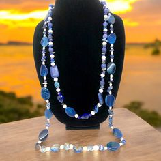 This stunning necklace measures 35 inches and features blue lapis lazuli, complemented with pearls, crystals, and iridescent stones. According to the Sumerians, the lapis lazuli stone housed the spirit of their gods, while the ancient Egyptians regarded it as a representation of the night sky. Lapis lazuli has always been connected to qualities such as strength, courage, intelligence, truth, royalty, and wisdom since ancient times. This necklace can brighten up any room with its bedazzling sparkle. Wrap it three times with the lighter-colored stones at the bottom. Blue Kyanite Jewelry With Gemstone Beads, Blue Kyanite Gemstone Beads Jewelry, Blue Long Hand-strung Necklace, Blue Hand-strung Long Necklace, Blue Double Strand Beaded Necklace With Natural Stones, Sapphire Beaded Necklaces With Natural Lapis Lazuli Stones, Bohemian Blue Pearl Necklace With Gemstone Beads, Blue Bohemian Pearl Necklace With Gemstone Beads, Spiritual Blue Agate Necklace