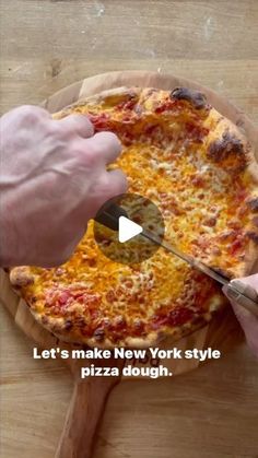 a person cutting a pizza on top of a wooden table