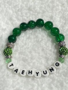 "The stage calls him V- but we know him as Tae! Don't miss out! BTS Taehyung Crackle Glass beaded bracelet in green to represent his mic color, with green and silver pavé accents. Letters are printed porcelain- NO PLASTIC. Size: 7.5\" stretches to fit most wrists comfortably." Trendy Green Crystal Round Beads Bracelet, Trendy Green Crystal Bracelet With Round Beads, Green Name Bracelet With Letter Beads, Trendy Green Beaded Bracelets With Letter Beads, Trendy Green Beaded Crystal Bracelet, Trendy Green Name Bracelet For Gift, Trendy Personalized Green Name Bracelet, Green Personalized Bracelets With Round Beads, Personalized Green Trendy Bracelets