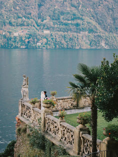 a bride and groom standing on the edge of a stone bridge overlooking a body of water