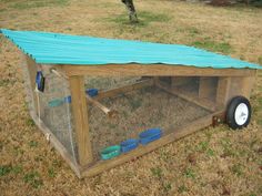 a chicken coop with a blue tarp on top and wheels attached to the roof