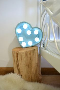 a heart shaped light sitting on top of a wooden stump next to a white bed