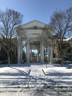 a white building with columns and pillars in the middle of snow covered ground next to trees