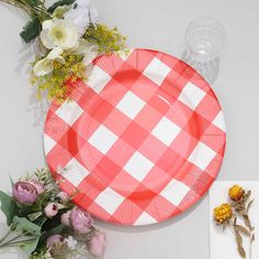 a red and white checkered paper plate next to flowers on a table with napkins