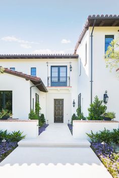 the front entrance to a white house with blue shutters and plants on either side