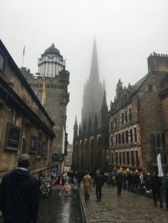 people are walking down the street in front of old buildings on a foggy day