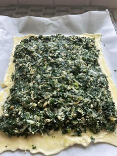 an uncooked pizza with cheese and spinach on it sitting on a piece of parchment paper