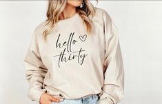 Gorgeous 30th Birthday sweater with the logo 'hello thirty' printed on it. Comes in white, sand and pink colour. Would make a perfect 30th birthday birthday gift for that special someone.  Crewneck sweatshirt is made of a blend of 50% cotton and 50% polyester.  Chose the appropriate size from the size chart provided. Or size up one or two sizes for the popular oversized look.  ⭐ To ensure longevity, we recommend -  *Turning item inside out to wash. *Machine was in cold water *Do not iron on prin White Relaxed Fit Sweatshirt For Birthday, Birthday Long Sleeve Sweatshirt With Lettering, White Sweatshirt With Name Print For Birthday, Hello Thirty Birthday, Custom Text Crew Neck Sweatshirt For Birthday, White Sweatshirt With Name Print, Relaxed Fit, Hello Thirty, Birthday Sweater, Birthday Sweatshirt