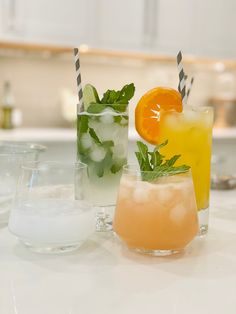 three different types of drinks sitting on a table with ice and orange slices in them