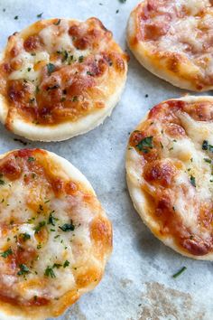 four small pizzas sitting on top of a piece of wax paper covered in cheese and herbs