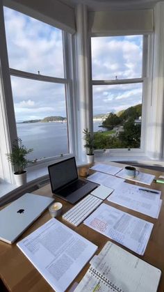 an open laptop computer sitting on top of a wooden desk in front of large windows