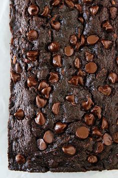 a close up of a chocolate brownie on a piece of parchment paper with chocolate chips