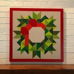 a wall hanging on the side of a white brick building with a green and red geometric design