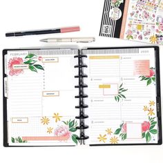 an open planner with flowers on it next to a pen