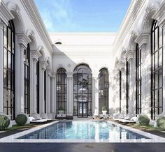 an indoor swimming pool surrounded by white columns and black framed windows with glass doors on both sides