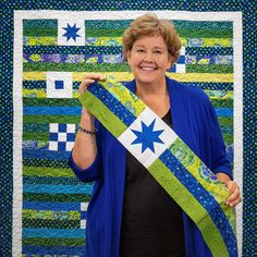 a woman holding up a blue and green quilt