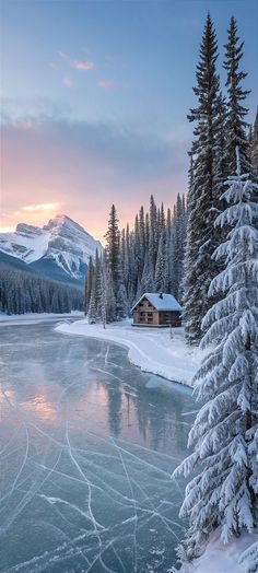 a lake surrounded by snow covered trees with a cabin in the background at sunset or dawn