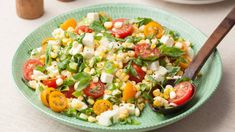 a salad with tomatoes, corn and feta cheese in a green bowl on a table