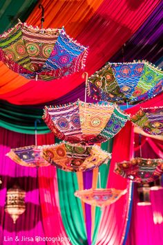 colorful umbrellas hanging from the ceiling in front of draping with lights on them