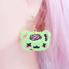 "Unleash your playful and quirky side with our kawaii plush zombie bear earrings! Crafted from bright green minky fabric, these adorable yet spooky earrings feature embroidered faces and carefully stitched black details, creating a cute and undead charm. The 18kt gold-plated earwires add a touch of luxury, making these earrings a unique accessory for those who appreciate the extraordinary. Handmade in the USA, each pair is crafted in my studio, ensuring attention to detail and quality. The brigh Harajuku Style Halloween Jewelry Gift, Cute Handmade Halloween Earrings, Handmade Green Kawaii Earrings, Zombie Bear, Bear Anime, Embroidered Faces, Spooky Earrings, Anime Earrings, Bear Earrings