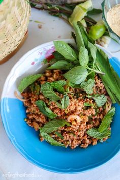 a blue plate topped with meat and greens on top of a white table next to other food items