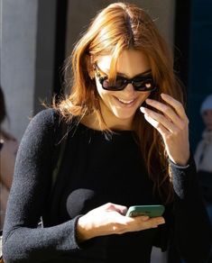 a woman in black shirt and sunglasses holding a cell phone to her ear while walking down the street