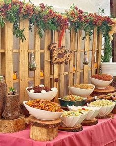 a table topped with lots of bowls filled with food next to a wooden fence covered in flowers