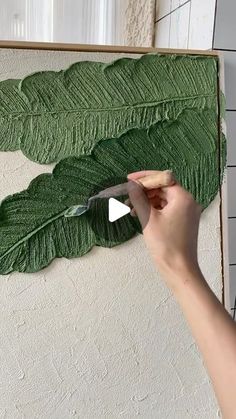 a person is cutting leaves with a knife on a canvas that has been painted green