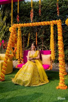 a woman in a yellow dress sitting on a pink bench with flowers hanging from it