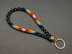 a multicolored lanyard with a gold ring on a gray background, the lanyard is made out of braiding and beads