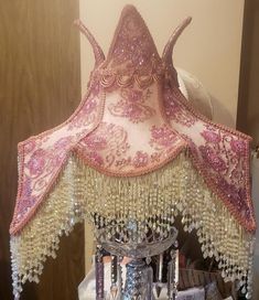 a lamp that is sitting on top of a table in front of a mirror with beads hanging from it's sides