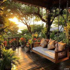 a porch swing with pillows on it in front of trees and flowers at sunset or dawn