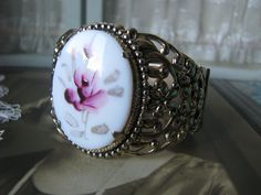 A beautifully ornate gold washed floral filigree painted glass rose cameo hinged bangle bracelet. The cameo measures 1 5/8'' x almost 1 1/4''. The bracelet measures 1 7/8'' at the widest. Also measures 2 1/2'' x 2 1/8'' across, and 7 5/8'' along the inside. In very good condition with subtle subduing of the gold. revealing the cool shiny silver underneath. Cameo Bracelet, Floral Filigree, Filigree Bracelet, Glass Rose, Vintage Cameo, Gold Wash, Painted Glass, Hinged Bangle, Shiny Silver