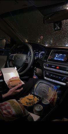 a person sitting in the driver's seat of a car with food and drinks