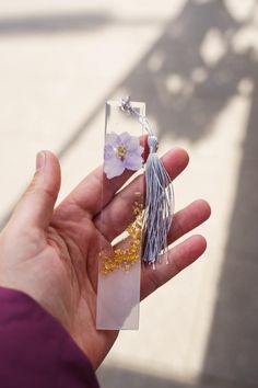 a hand holding a piece of glass with flowers on it and some tassels