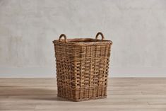 a wicker basket with handles on a wooden floor in front of a white wall