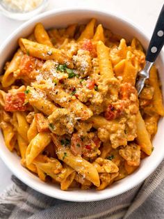 a white bowl filled with pasta and meat covered in sauce on top of a table