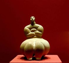 a sculpture of a woman sitting on top of a red block in front of a red wall