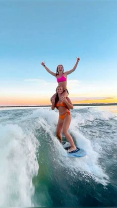 two girls are riding on the back of a surfboard