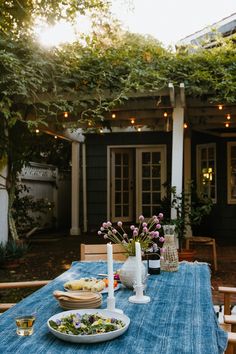 a blue table cloth with plates and bowls on it in front of an outdoor dining area